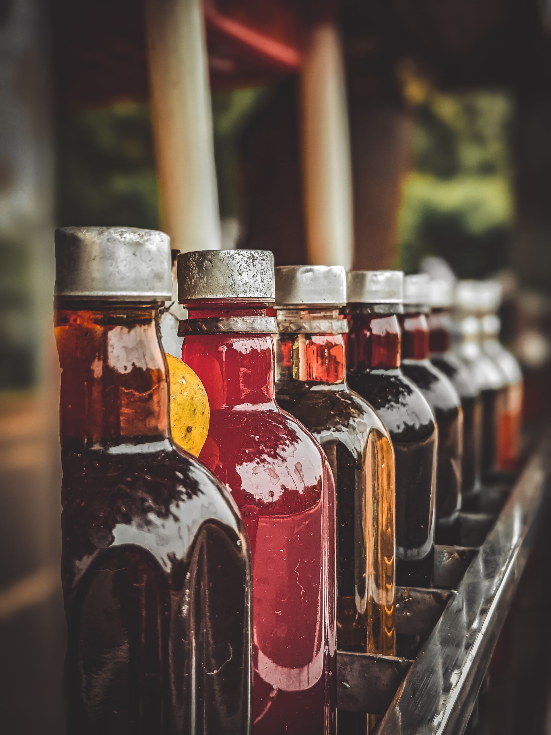 A row of vibrant and assorted bottles displaying various liquids, photographed outdoors.